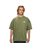 Person wearing a green t-shirt with a small logo on a white background