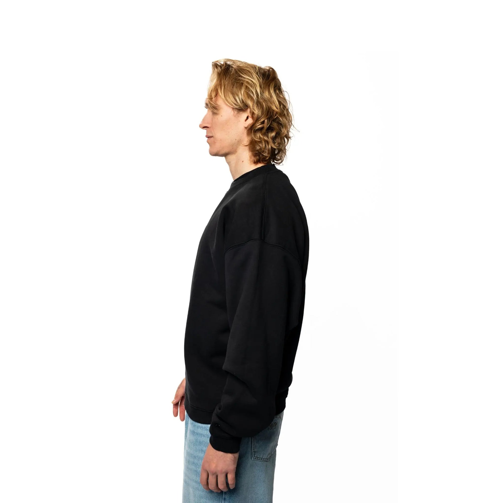 Person wearing a black sweatshirt and blue jeans on a white background